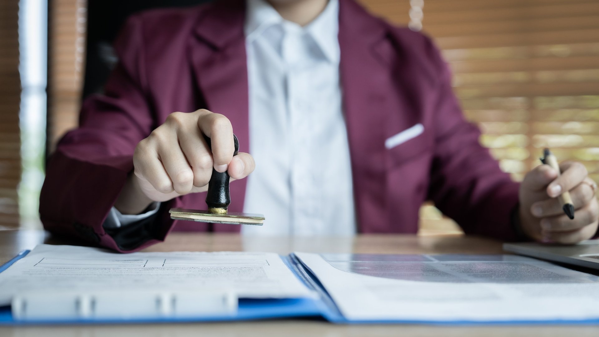 A man in a suit is stamping a document with a stamp. The stamp is black and gold